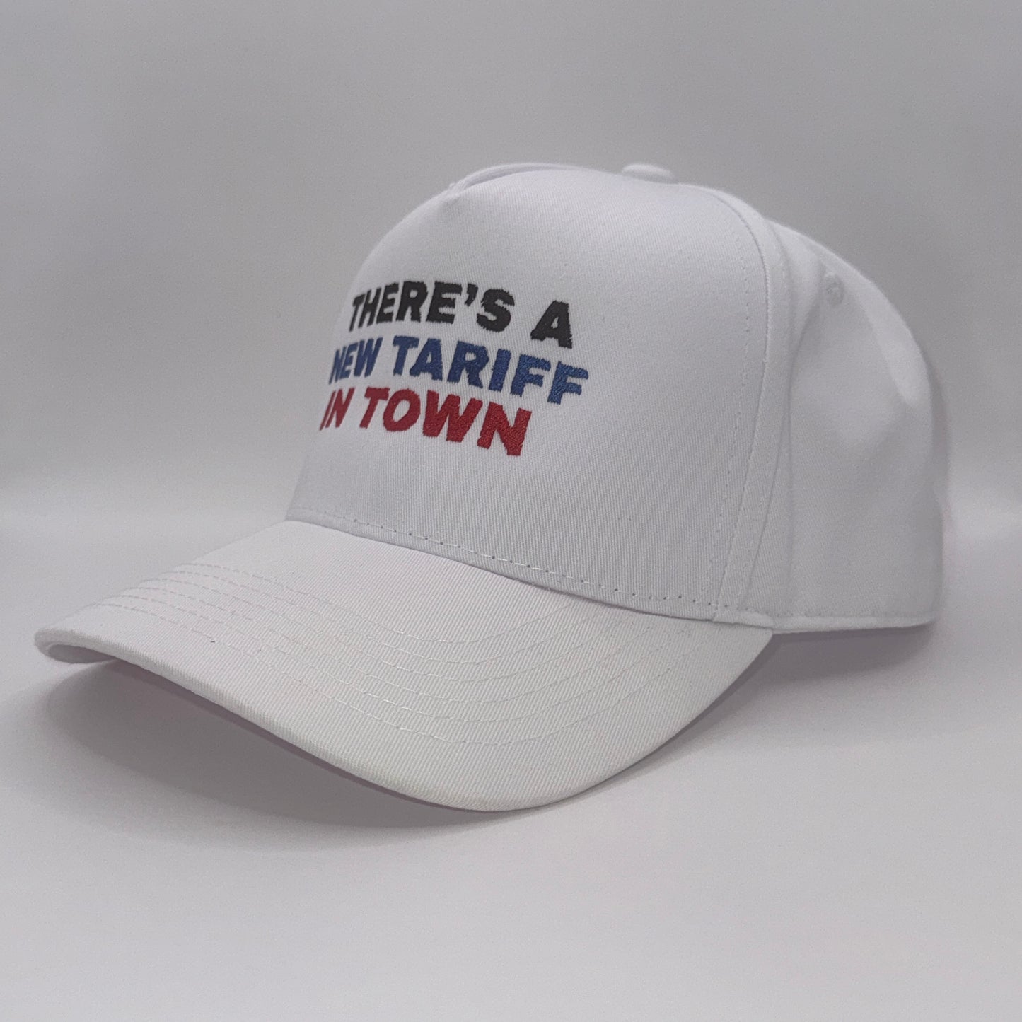 “White snapback hat with embroidered text ‘There’s a new tariff in town’ in black, blue, and red”