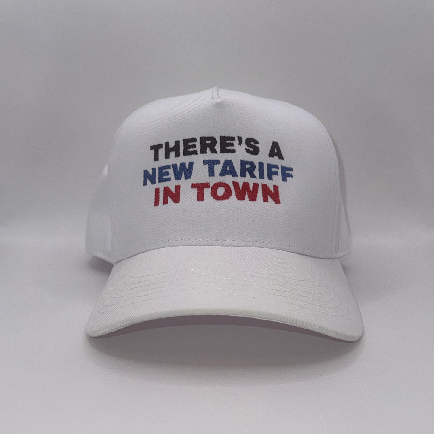 “White snapback hat with embroidered text ‘There’s a new tariff in town’ in black, blue, and red”
