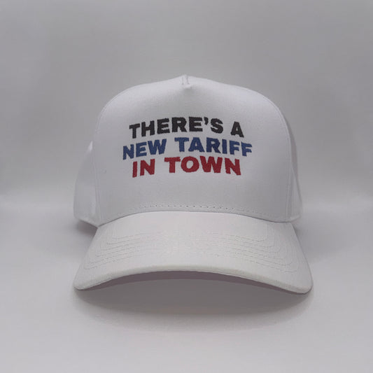 “White snapback hat with embroidered text ‘There’s a new tariff in town’ in black, blue, and red”