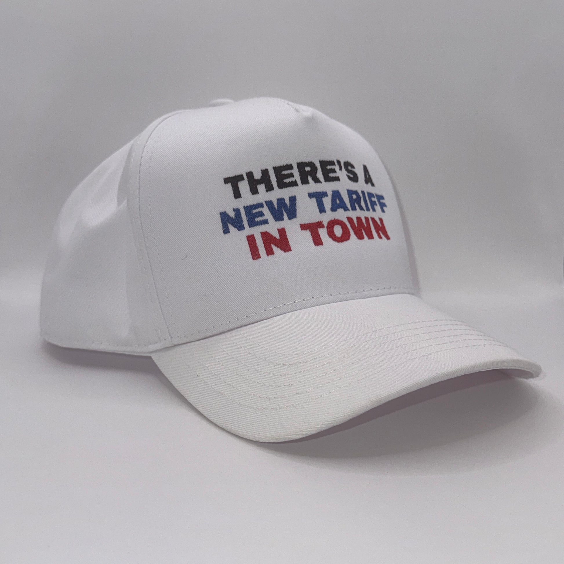 “White snapback hat with embroidered text ‘There’s a new tariff in town’ in black, blue, and red”