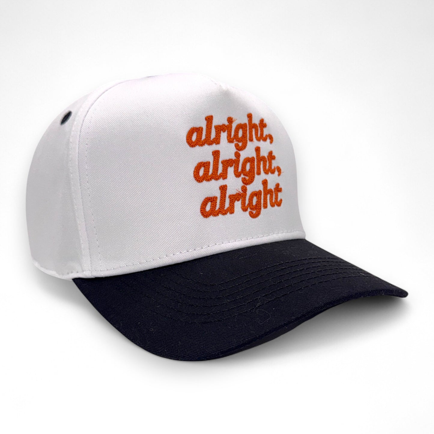 Angled side view of white hat with black bill and orange embroidered text